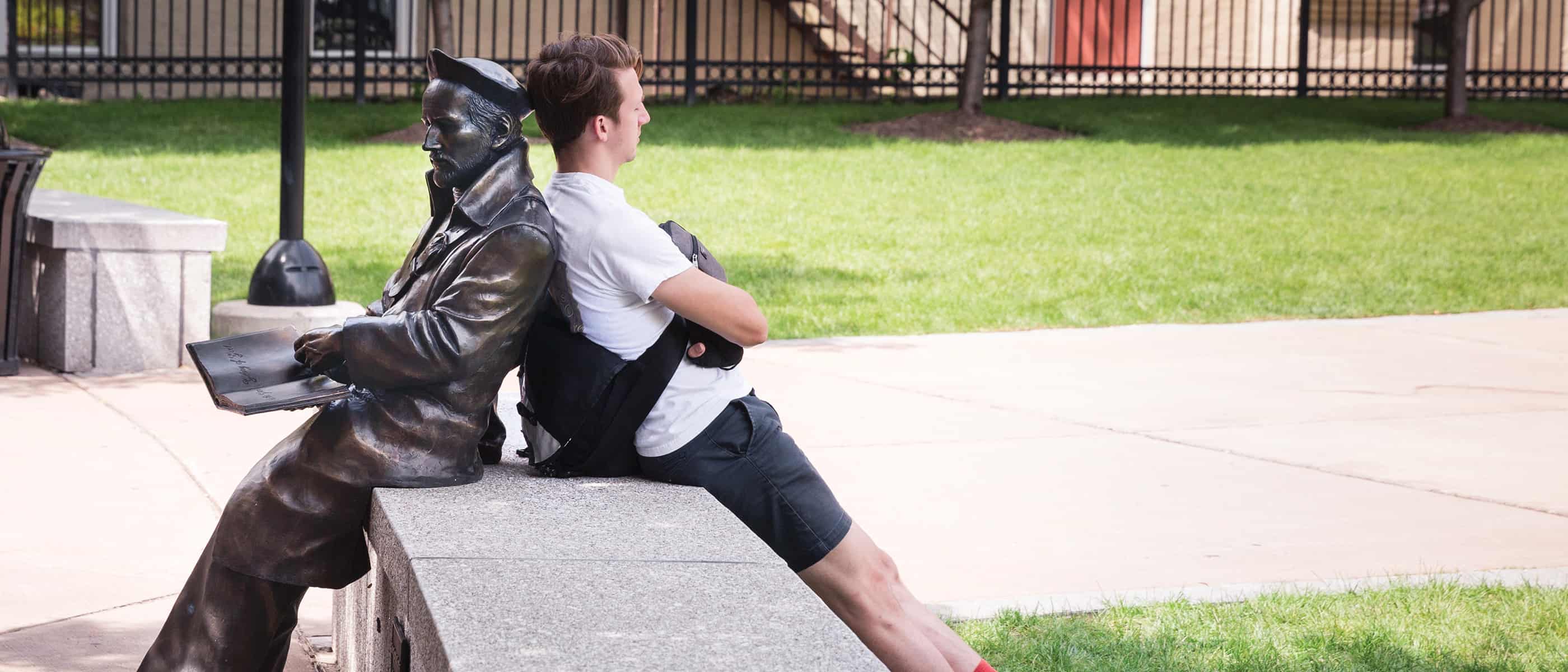 student relaxing in front of the MacMahon Center leaning against the stature of SAʴý Ignatius Loyola